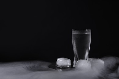 Photo of Vodka in shot glass with ice on black table against dark background, space for text