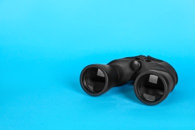 Photo of Modern binoculars on light blue background, space for text