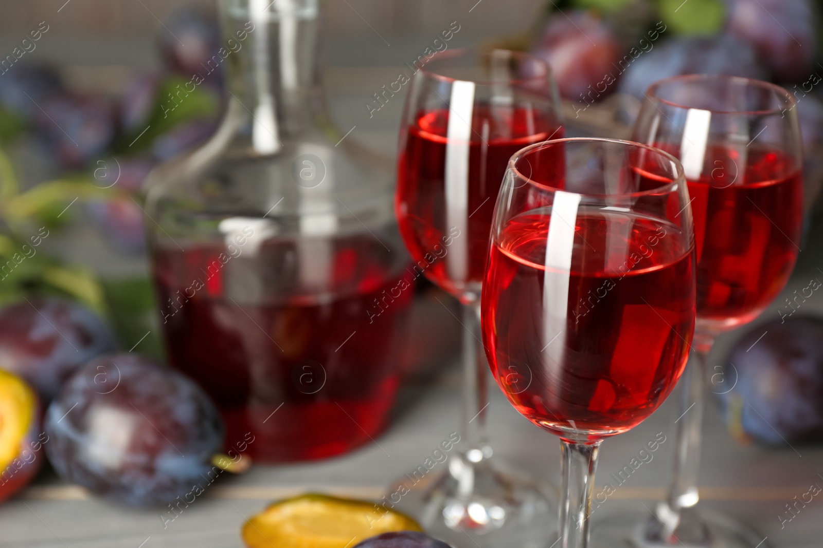 Photo of Delicious plum liquor and ripe fruits on table, closeup. Homemade strong alcoholic beverage