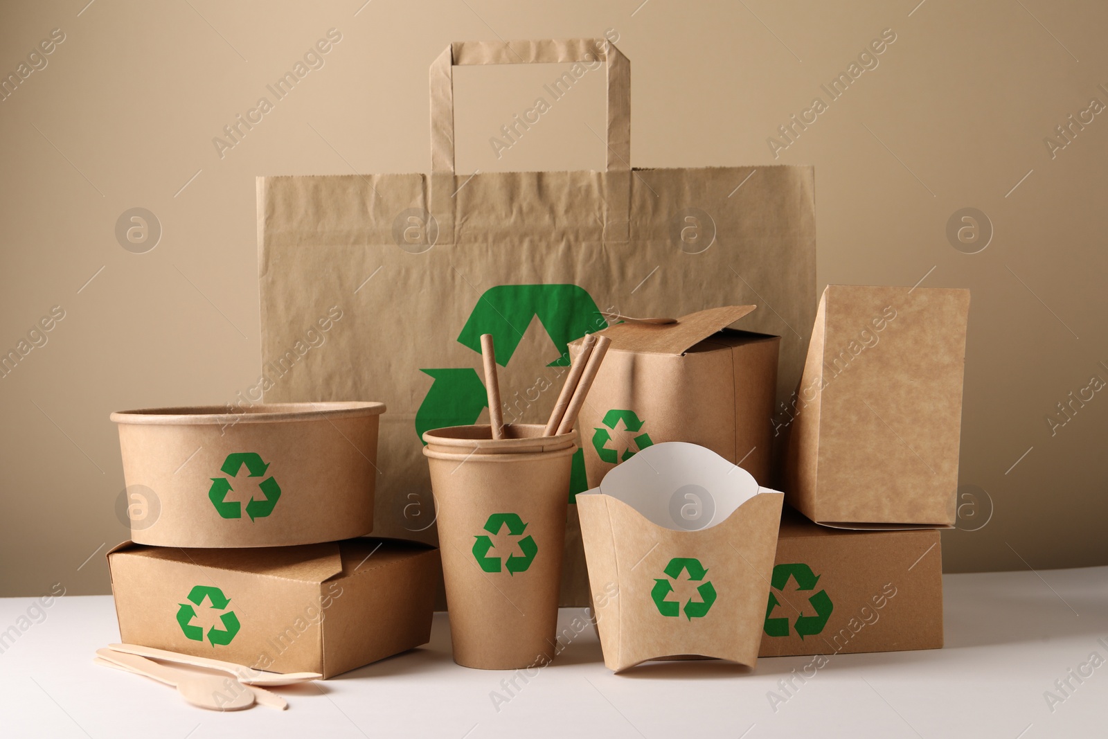 Image of Set of eco friendly food packaging with recycling symbols on white table against beige background