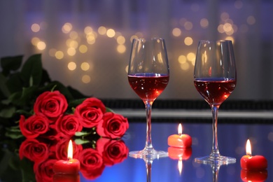 Photo of Glasses of wine, candles and roses on table against blurred lights. Romantic dinner for Valentine's day