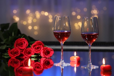 Glasses of wine, candles and roses on table against blurred lights. Romantic dinner for Valentine's day