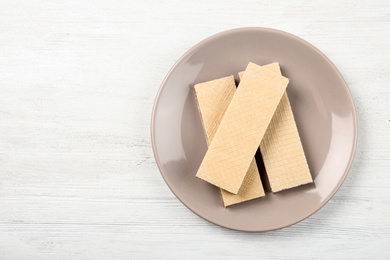 Plate with delicious crispy wafers on white wooden table, top view. Space for text