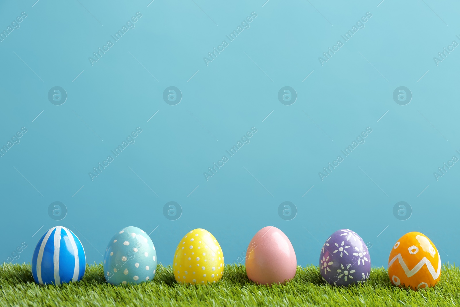 Photo of Painted Easter eggs on green grass against color background, space for text