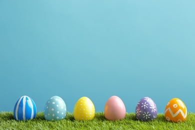 Painted Easter eggs on green grass against color background, space for text