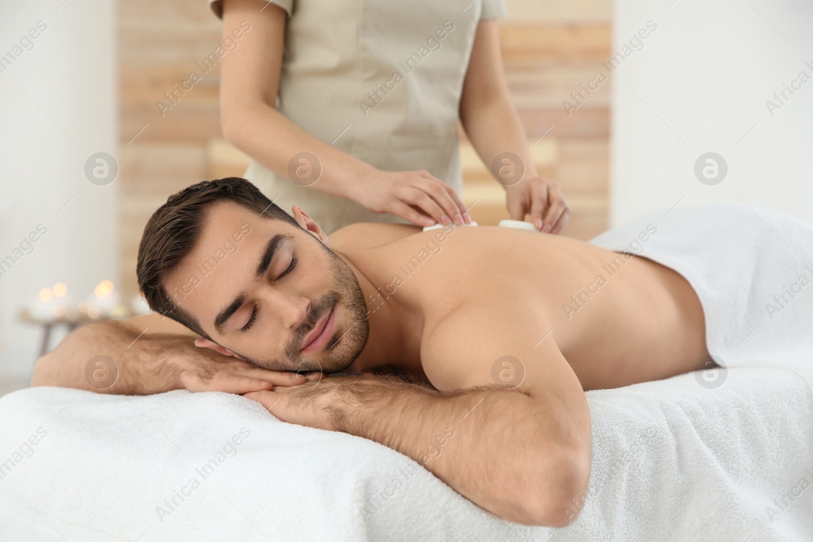 Photo of Handsome man receiving hot stone massage in spa salon