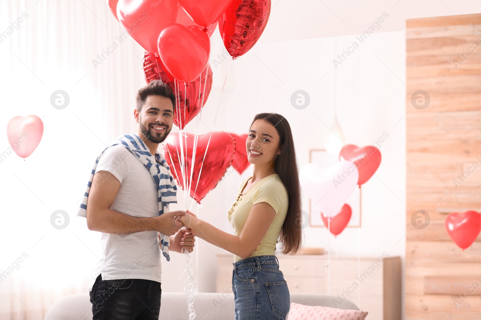 Photo of Happy young couple with heart shaped balloons in living room. Valentine's day celebration