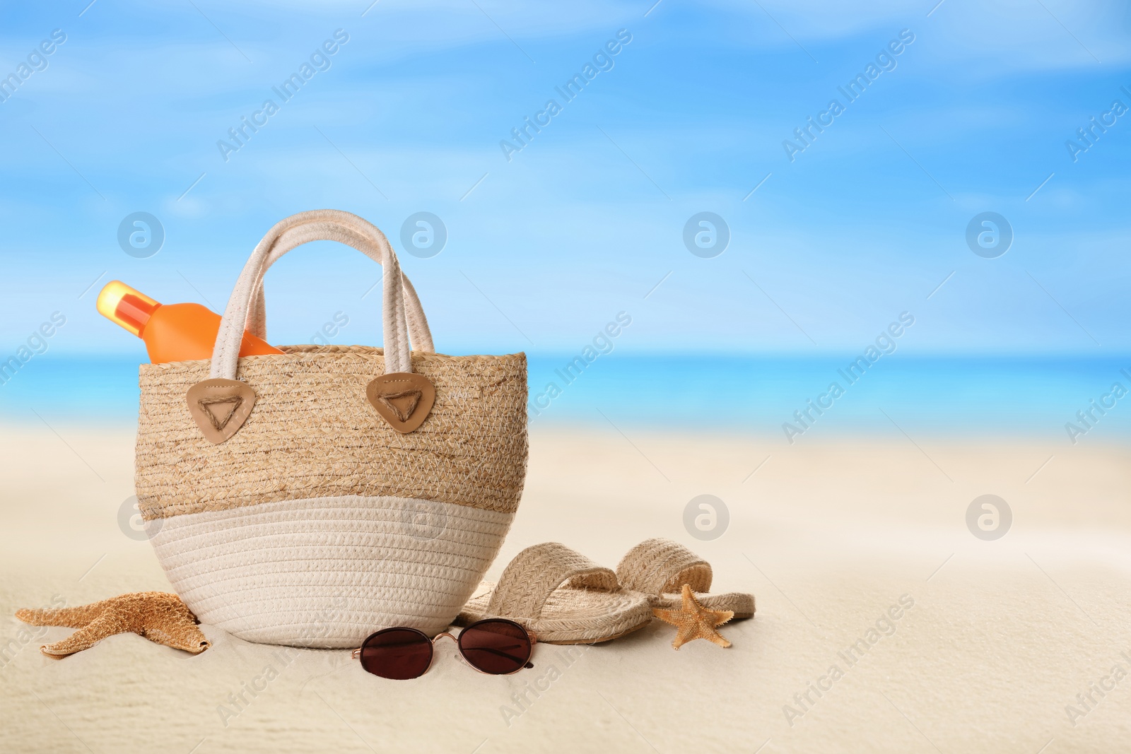 Image of Bag with sunscreen and accessories on sunny ocean beach, space for text. Summer vacation