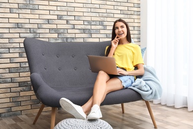 Young woman with modern laptop sitting on sofa at home