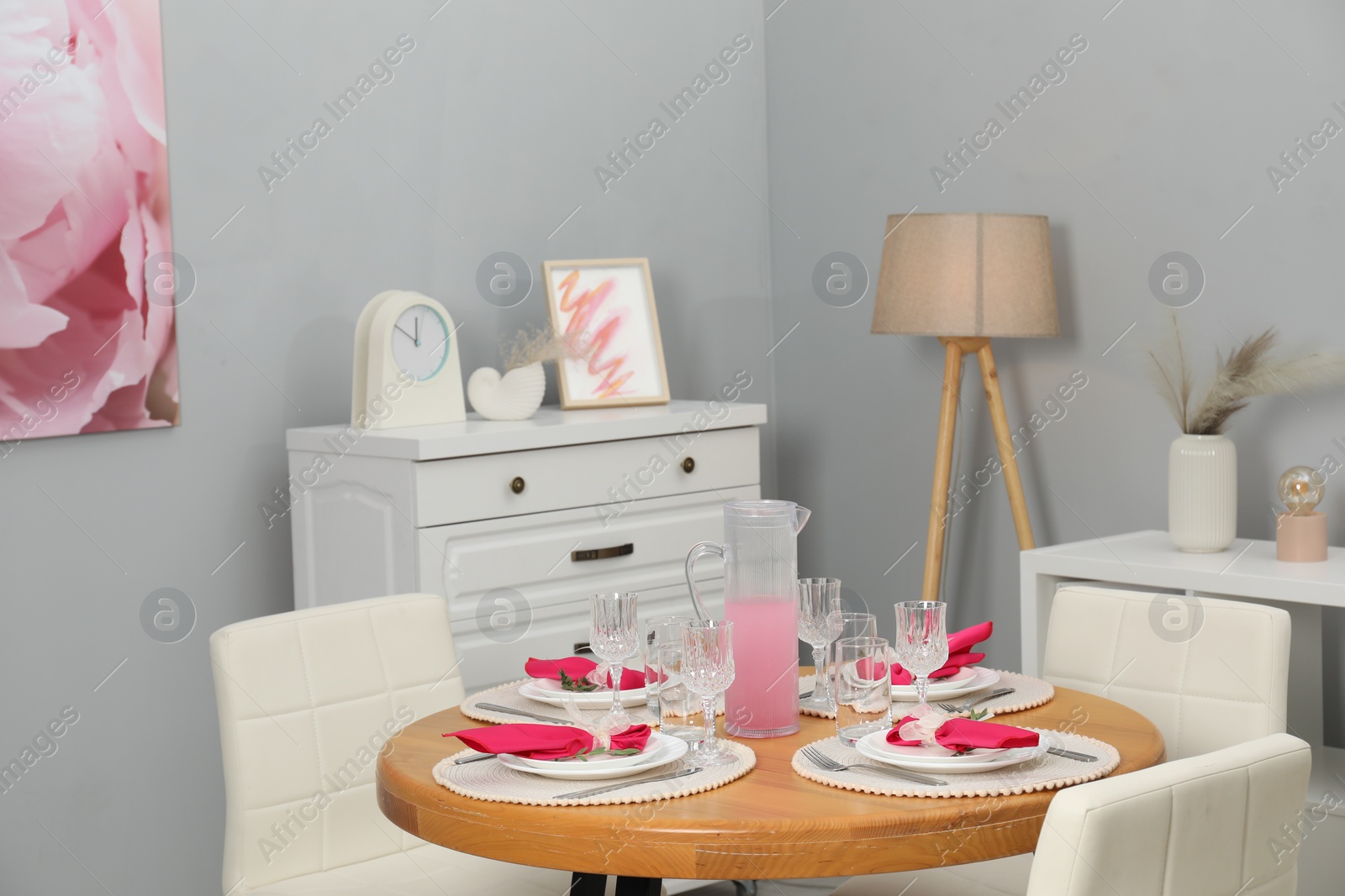 Photo of Color accent table setting. Glasses, plates, jug of beverage and pink napkins in dining room