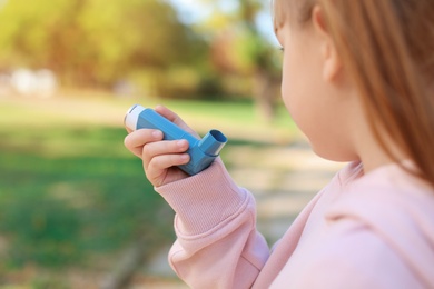 Photo of Little girl using asthma inhaler outdoors. Health care
