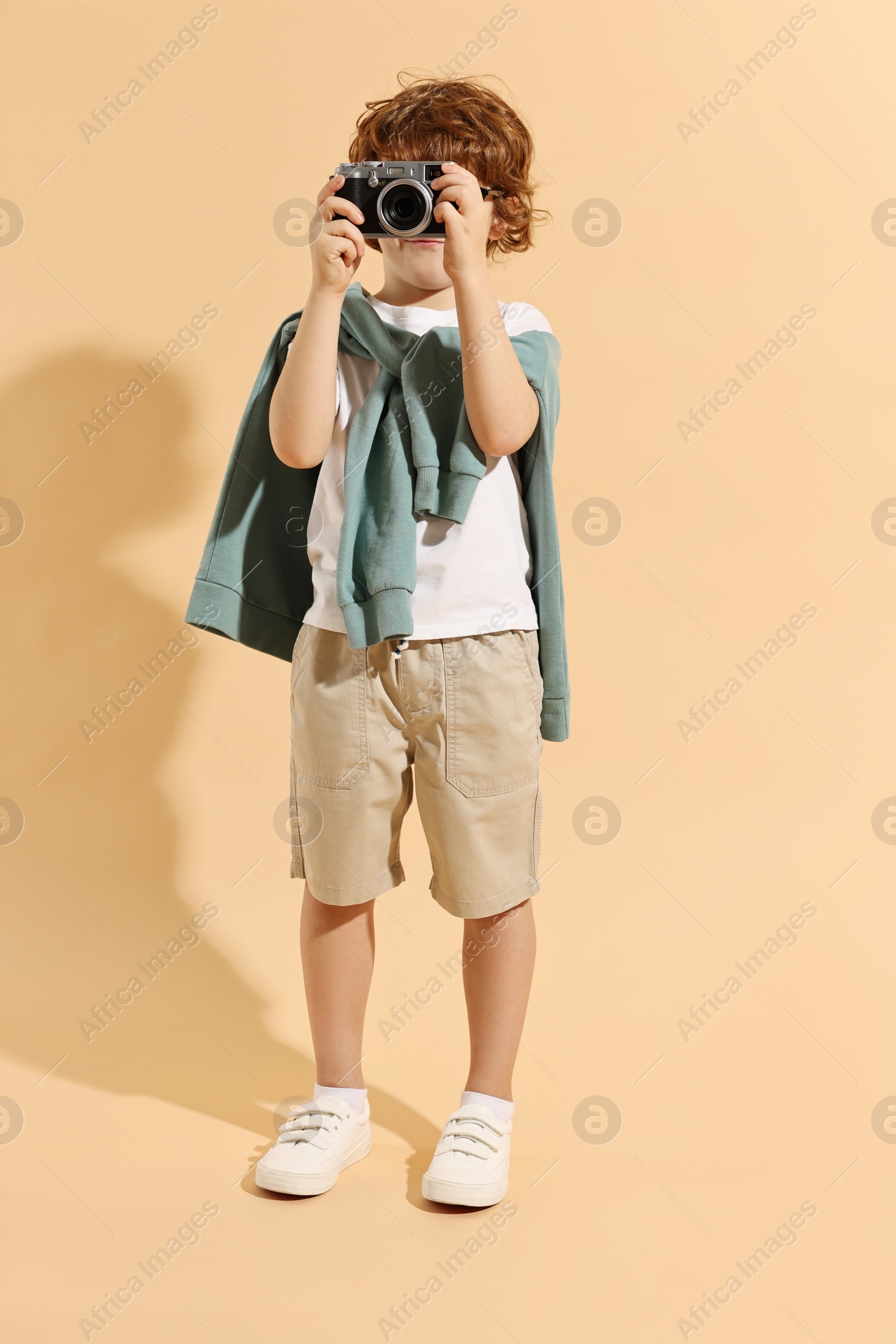 Photo of Fashion concept. Stylish boy with vintage camera on pale orange background