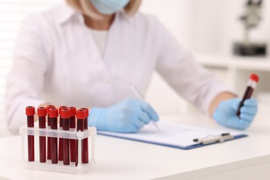 Photo of Doctor with samples of blood in test tubes at white table, selective focus