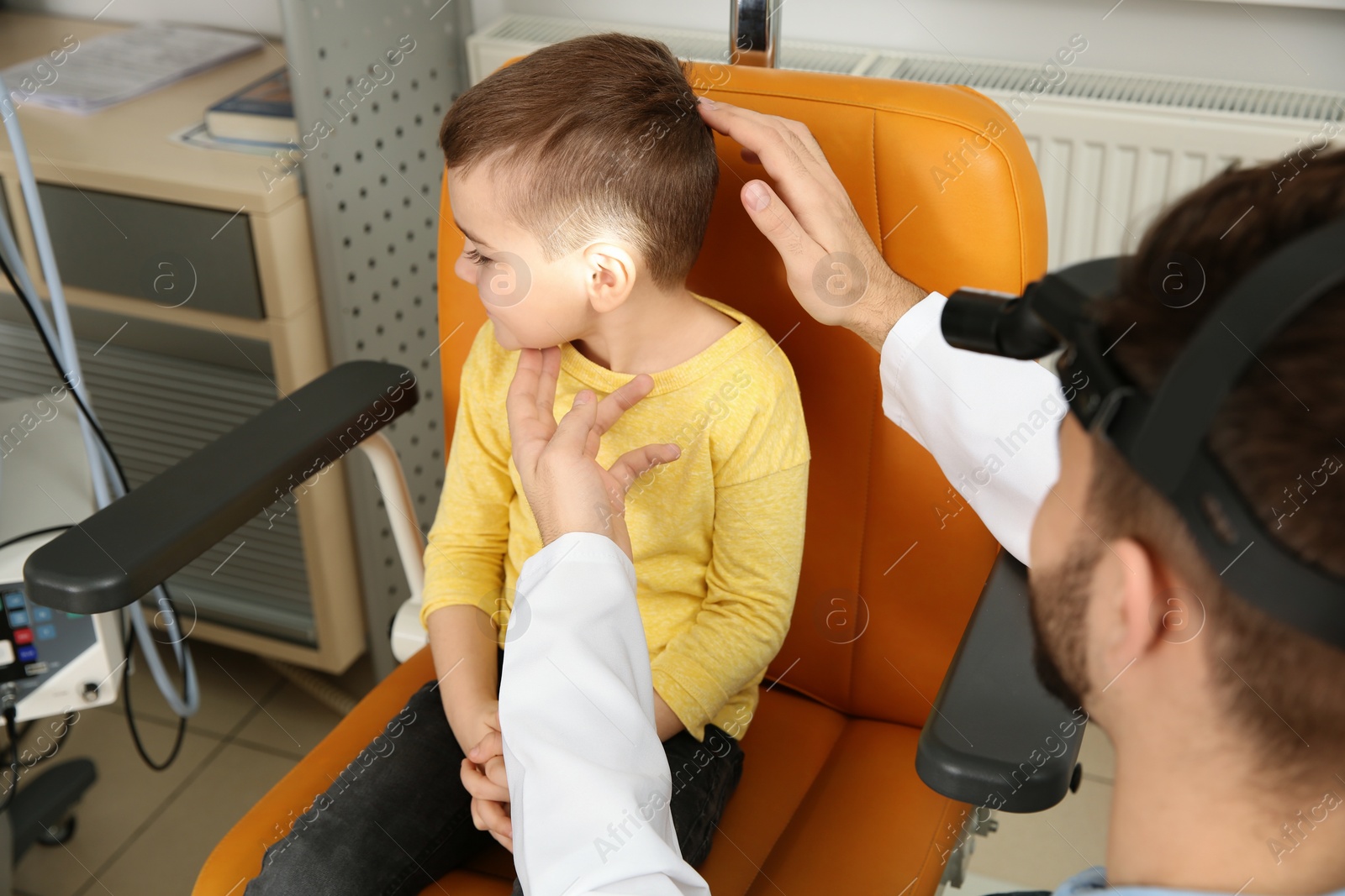 Photo of Professional otolaryngologist examining little boy in clinic. Hearing disorder