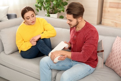 Photo of Young man applying bandage on woman's injured leg at home. First aid