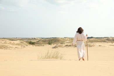 Photo of Jesus Christ walking with stick in desert, back view. Space for text