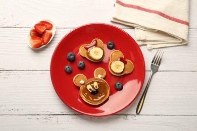 Photo of Creative serving for kids. Plate with cute bears made of pancakes, berries, banana and chocolate paste on white wooden table, flat lay