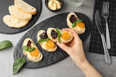 Photo of Woman eating tasty tomato bruschettas at table, flat lay