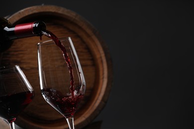 Pouring delicious wine into glass near wooden barrel against black background, closeup. Space for text