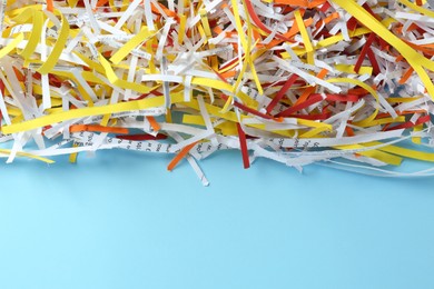Photo of Heap of shredded colorful paper strips on light blue background, closeup