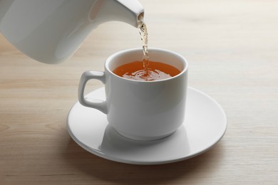 Pouring green tea into white cup with saucer on wooden table, closeup