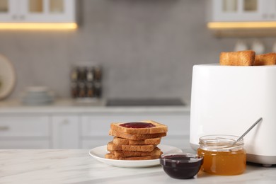 Photo of Making toasts for breakfast. Appliance, crunchy bread, honey and jam on white table in kitchen. Space for text