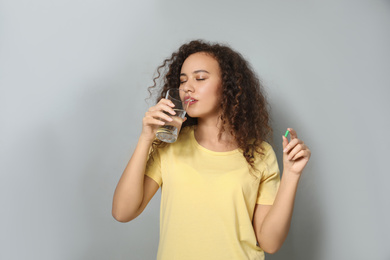 African-American woman with glass of water and vitamin capsule on light grey background