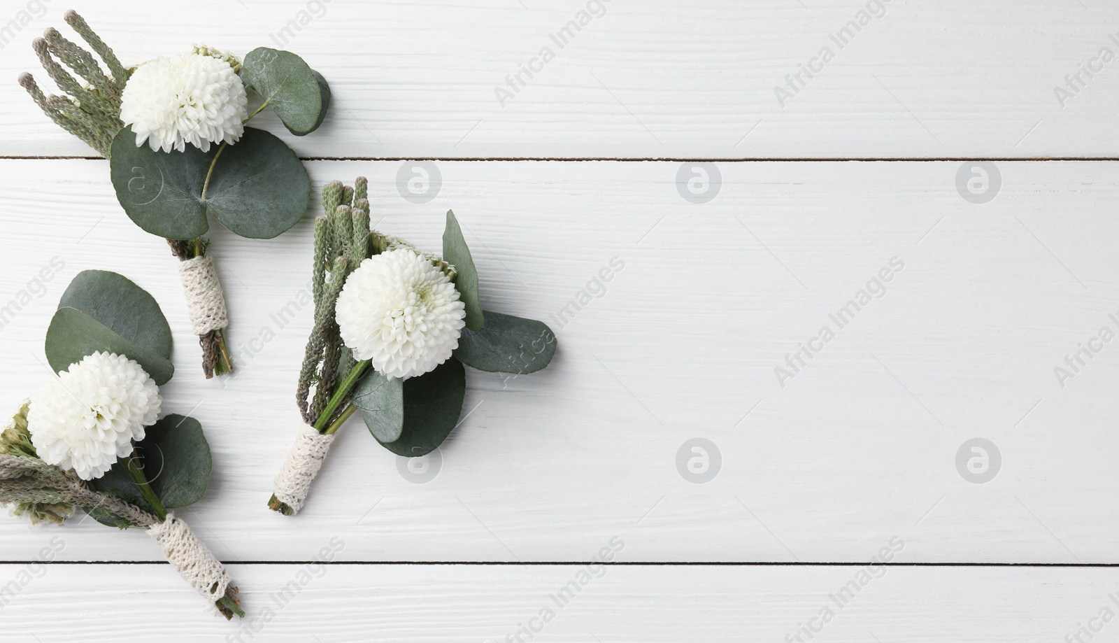 Photo of Small stylish boutonnieres on white wooden table, flat lay. Space for text