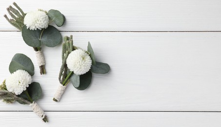 Photo of Small stylish boutonnieres on white wooden table, flat lay. Space for text
