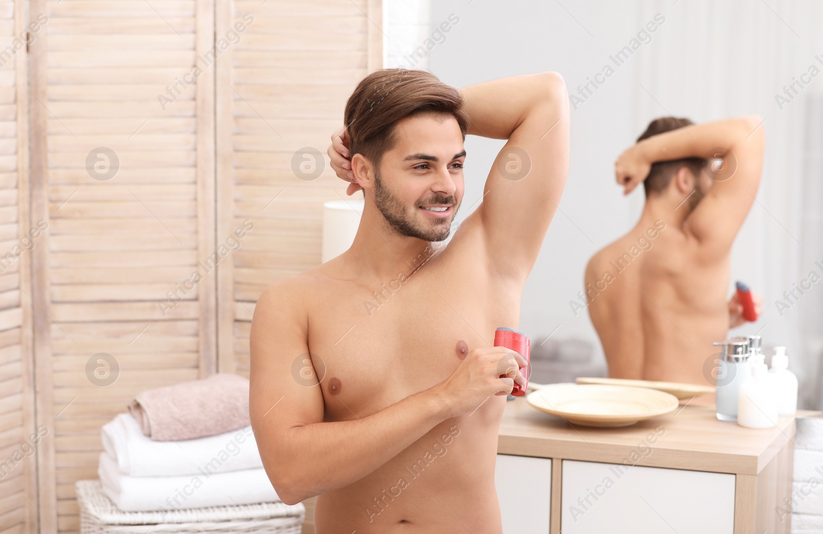 Photo of Handsome young man applying deodorant in bathroom