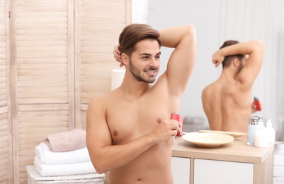 Handsome young man applying deodorant in bathroom