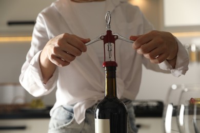 Photo of Woman opening wine bottle with corkscrew indoors, closeup