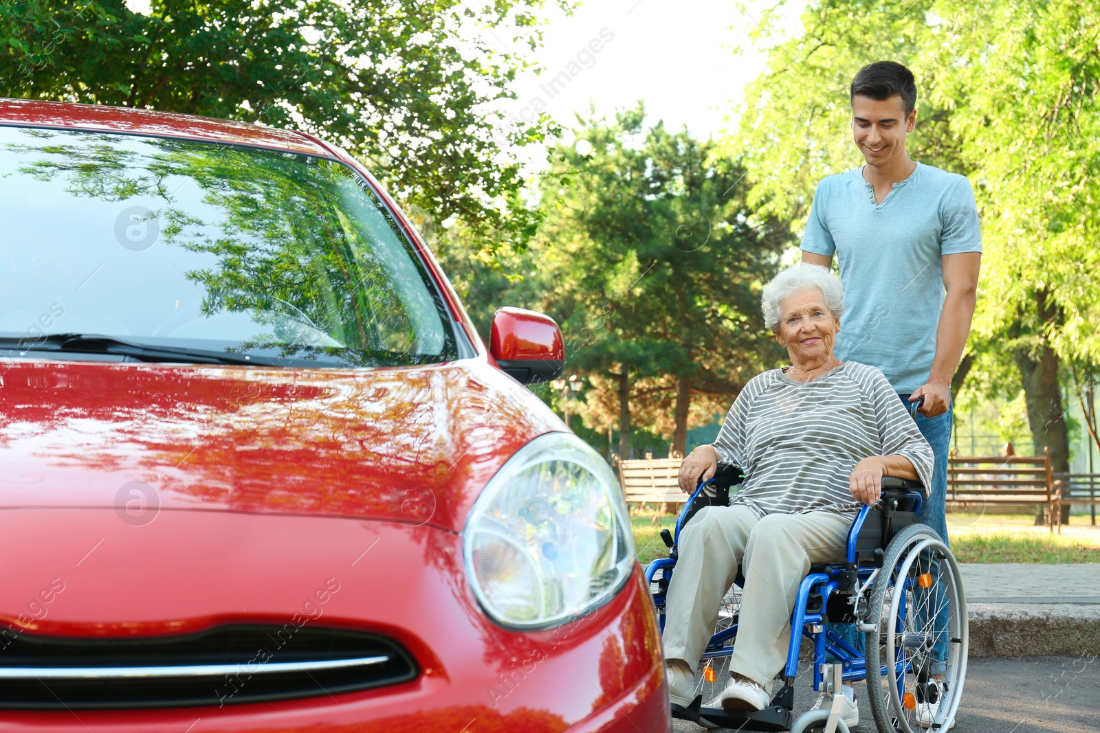 Photo of Young man with disabled senior woman in wheelchair near car outdoors