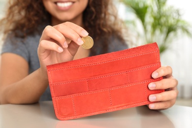 Woman putting coin into wallet at table, closeup