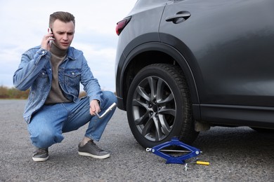 Photo of Worried young man calling car service. Tire puncture