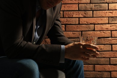 Addicted man with glass of alcoholic drink near red brick wall, closeup