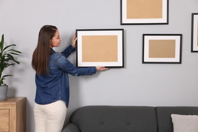 Woman hanging picture frame on gray wall at home