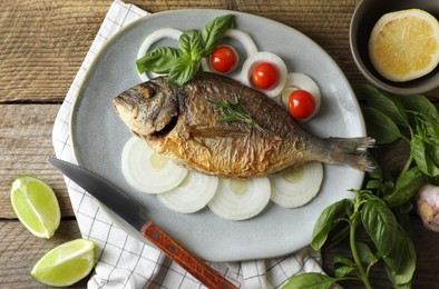 Delicious dorado fish with vegetables and herbs served on wooden table, flat lay