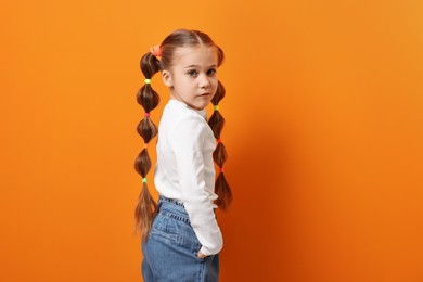 Cute little girl with beautiful hairstyle on orange background. Space for text