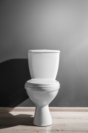 Photo of New ceramic toilet bowl near grey wall, side light