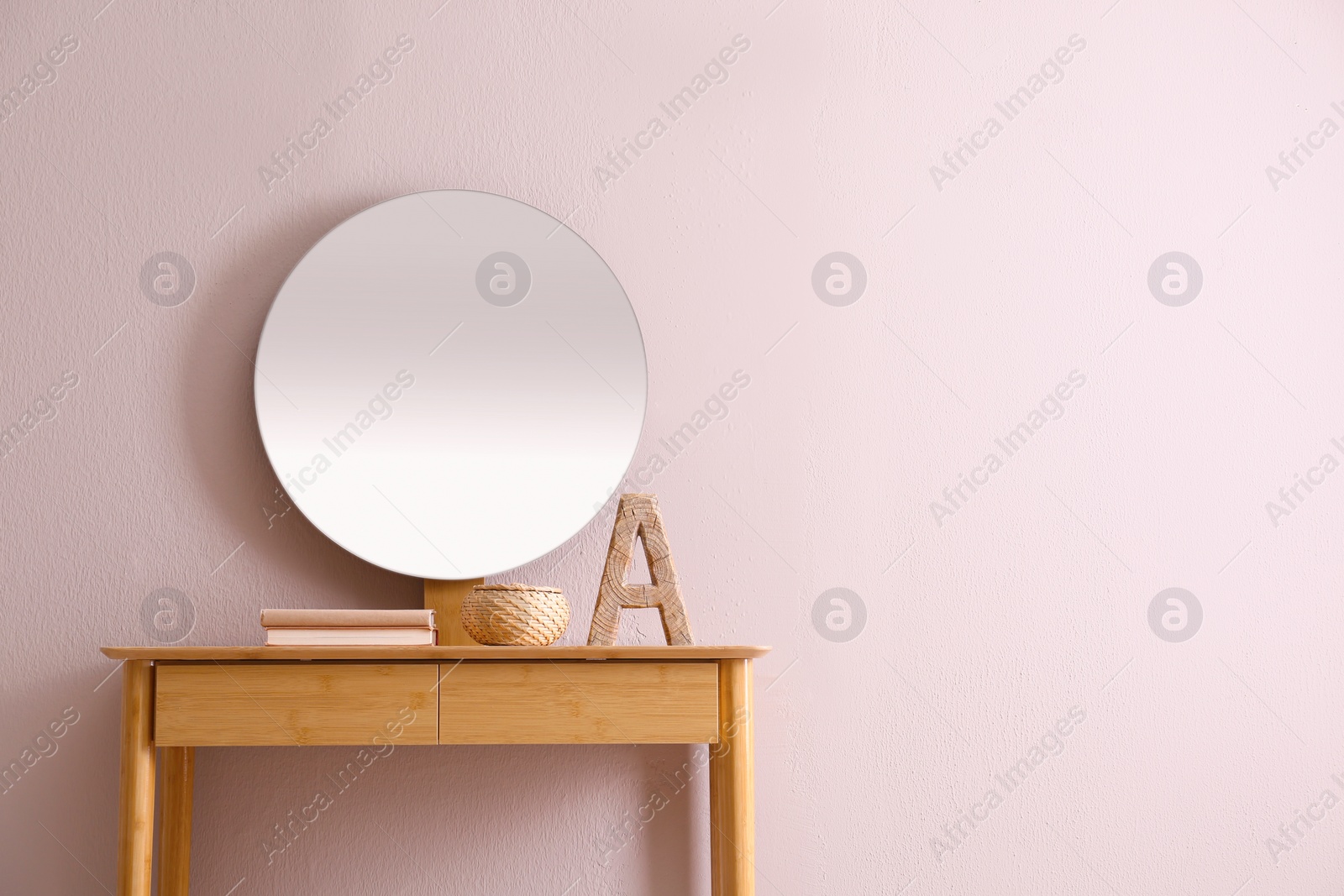 Photo of Books and decor on console table near beige wall with mirror indoors, space for text. Interior design