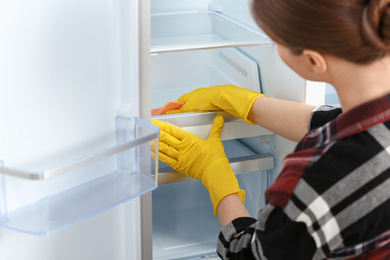 Woman in rubber gloves cleaning refrigerator, closeup