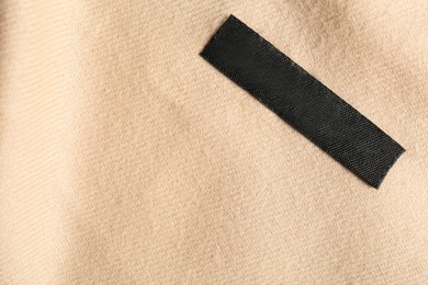 Photo of Blank clothing label on beige cashmere apparel, top view. Space for text
