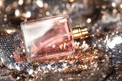 Photo of Luxury perfume in bottle on fabric with shiny sequins, closeup