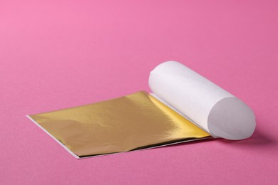 Photo of Edible gold leaf sheet on pink background, closeup. Space for text