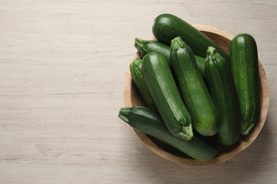 Raw ripe zucchinis in bowl on white wooden table, top view. Space for text