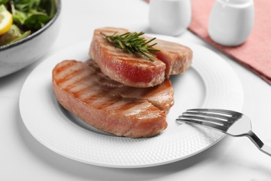 Delicious tuna steaks with rosemary on white table, closeup