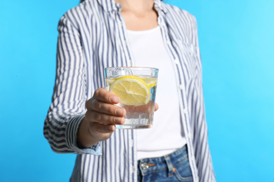 Photo of Young woman with glass of lemon water on light blue background, closeup