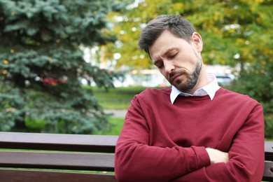 Tired man sleeping on bench in beautiful green park. Space for text