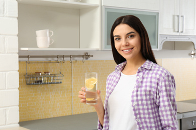 Photo of Beautiful young woman with lemon water in kitchen. Space for text